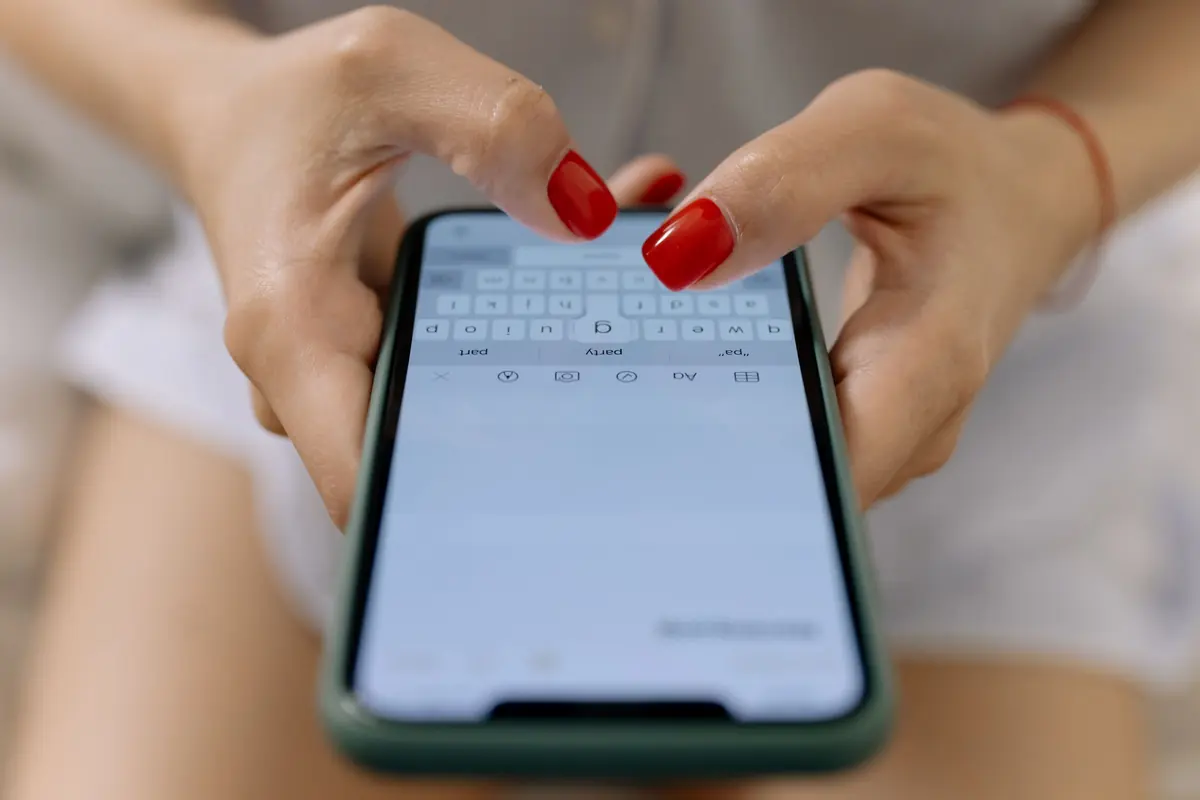 Руки з червоним манікюром набирають повідомлення на смартфоні